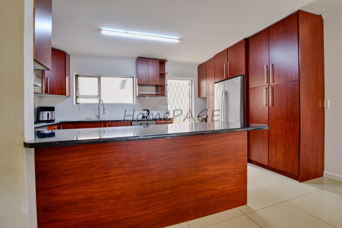 A spacious kitchen featuring dark wood cabinetry, granite countertops, and tiled flooring, offering a clean and functional layout.