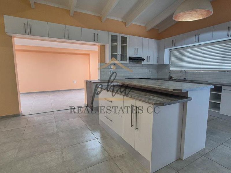 Spacious kitchen featuring a central island, ample built-in cabinetry, subway tile backsplash, and exposed beam ceilings, flowing into an adjacent living area.