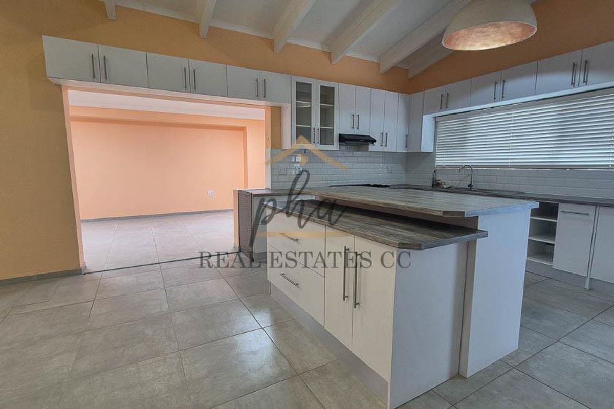 Spacious kitchen featuring a central island, ample built-in cabinetry, subway tile backsplash, and exposed beam ceilings, flowing into an adjacent living area.