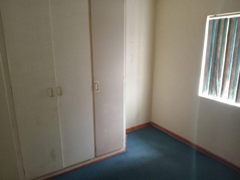 An empty bedroom featuring built-in cupboards, blue carpeting, and vertical window blinds. The room requires cosmetic updates to improve its overall condition.