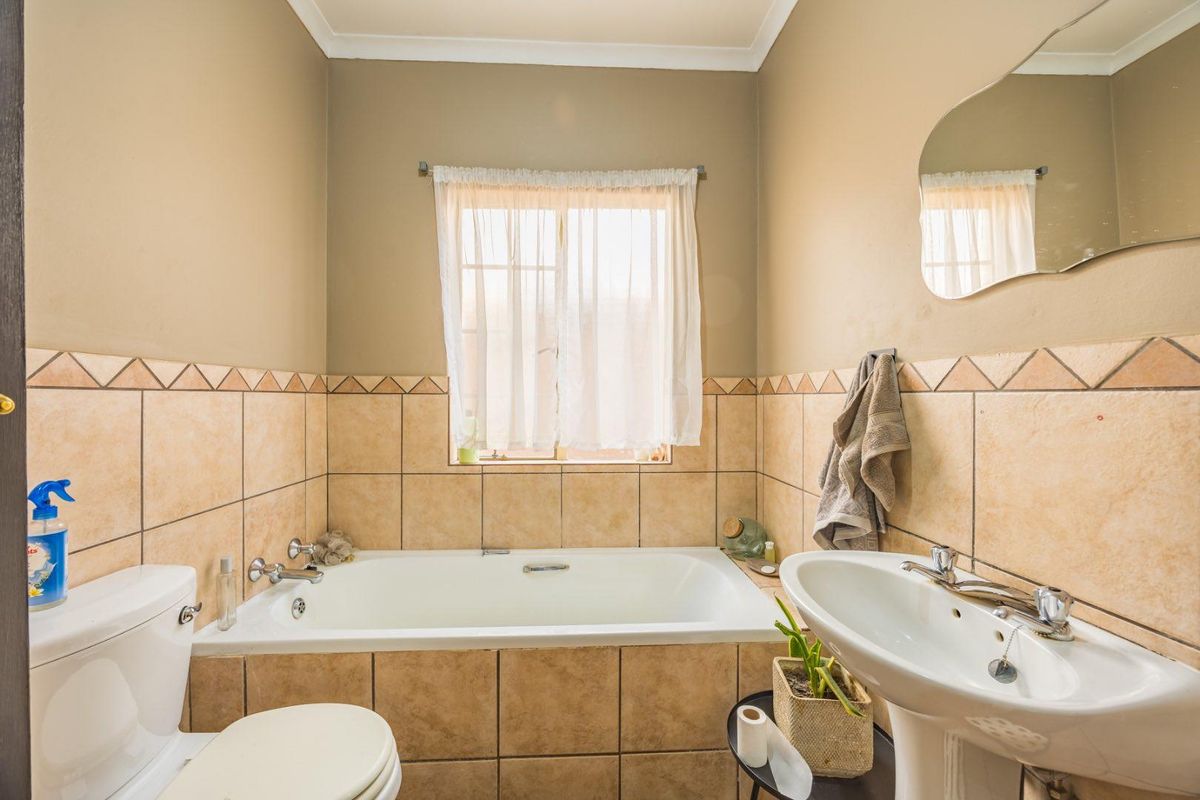 A functional bathroom featuring a built-in bathtub, pedestal washbasin, and toilet, finished with neutral ceramic wall tiles and a classic mirror.