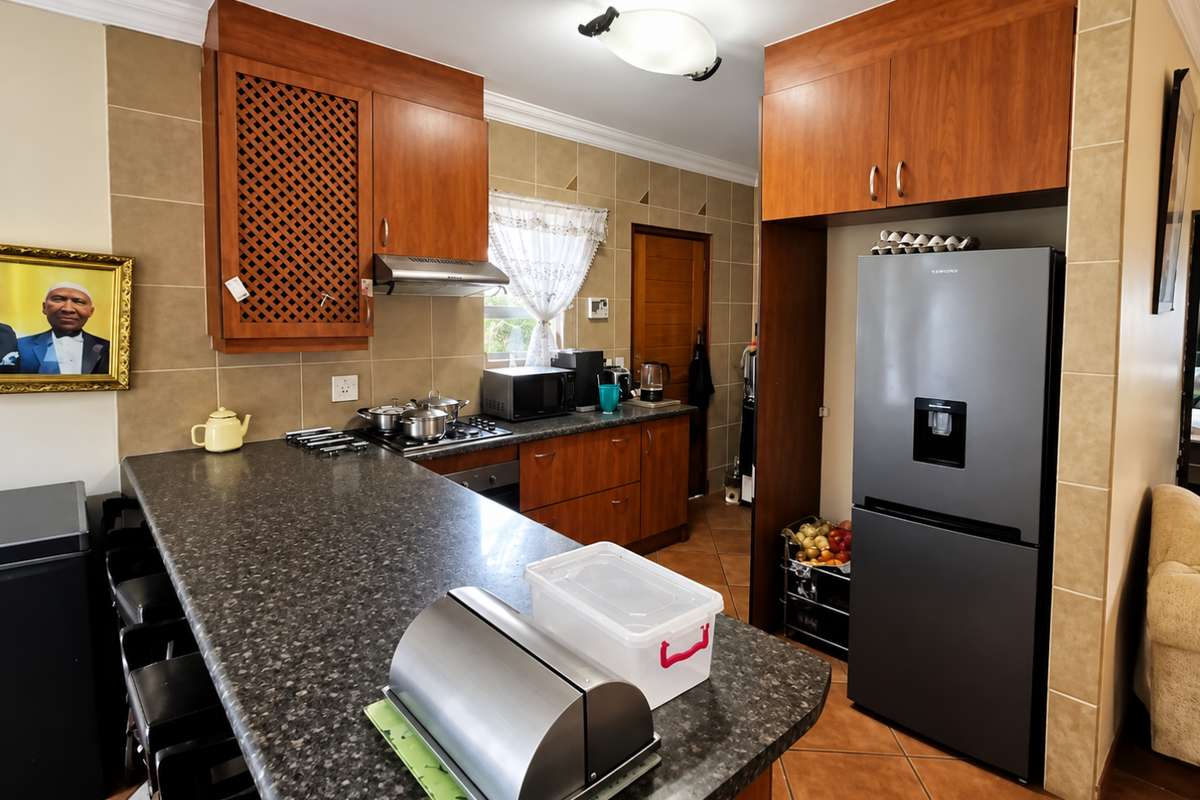 A functional kitchen featuring wood-finish cabinetry, granite countertops, a tiled backsplash, and integrated cooking appliances with a breakfast bar area.