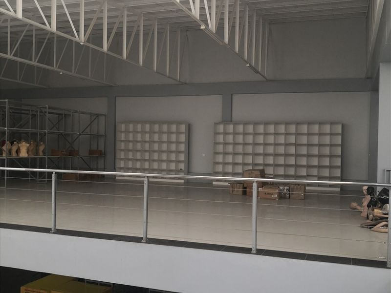 A spacious industrial mezzanine level featuring high steel truss ceilings, tiled flooring, and built-in shelving units, suitable for storage or office use.