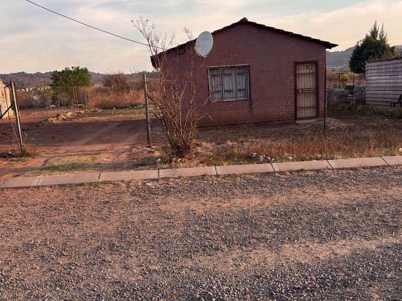 Front view of a detached residential property featuring a tiled roof, security gate, and security bars on windows, situated on an unpaved lot.