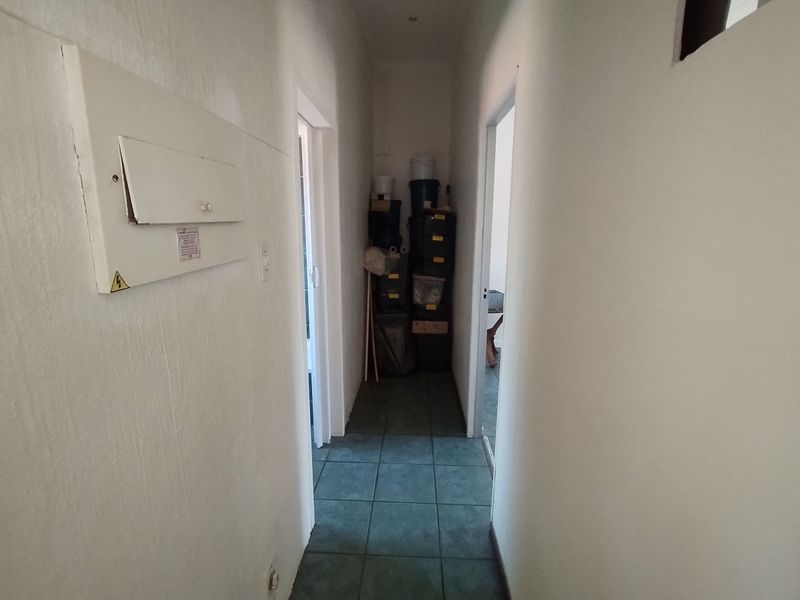 A narrow hallway featuring tiled flooring and a wall-mounted electrical distribution board, providing access to adjacent rooms.