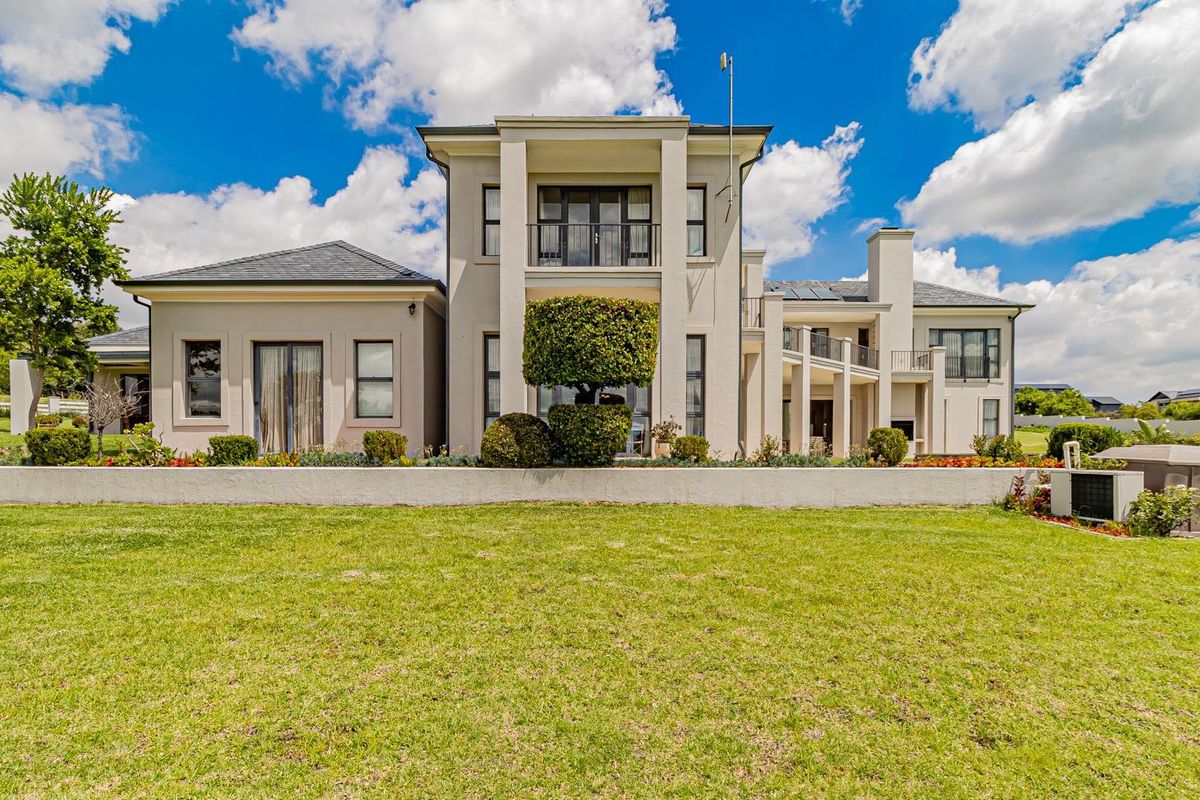 A grand double-story residence featuring a manicured lawn, expansive rear facade, multiple balconies, and well-maintained landscaping.