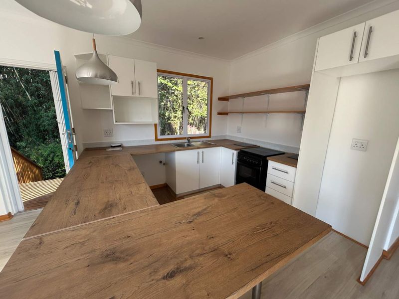 A bright, modern kitchen featuring wood-look laminate countertops, white cabinetry, open shelving, and direct access to an outdoor deck area.