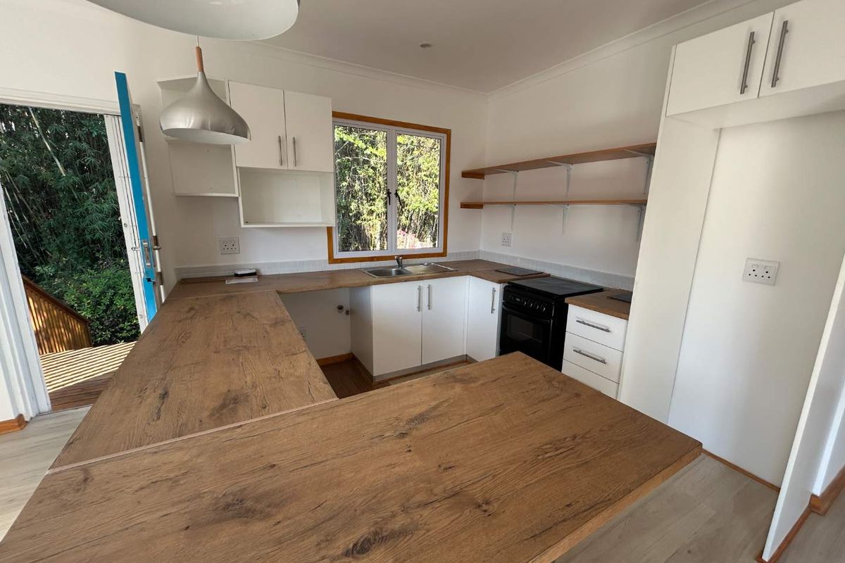 A bright, modern kitchen featuring wood-look laminate countertops, white cabinetry, open shelving, and direct access to an outdoor deck area.