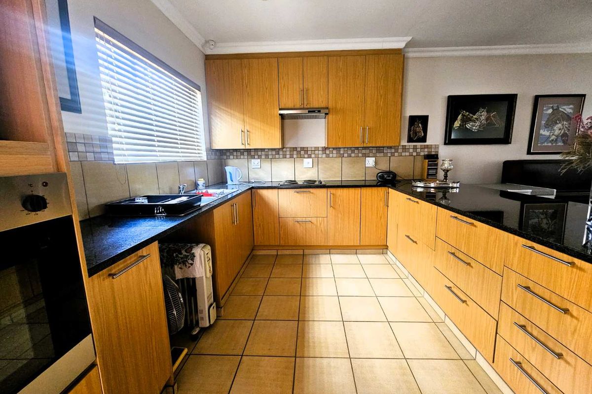 A functional U-shaped kitchen featuring light wood cabinetry, dark granite countertops, tiled backsplash, and built-in oven and hob.