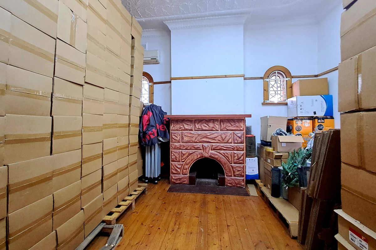 A living room featuring original timber flooring, an ornate fireplace, and decorative ceiling details, currently utilized for storage.