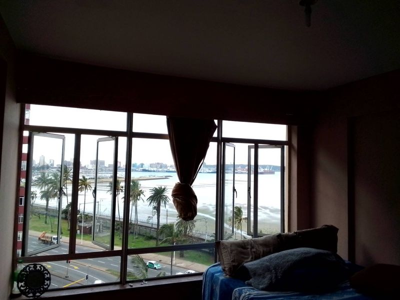 A view from an apartment window overlooking the coastal road, beach, and harbour area.