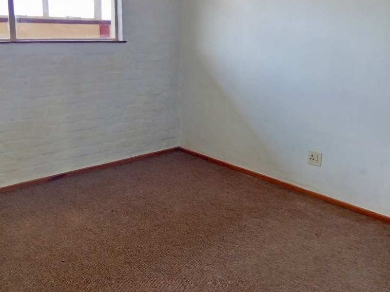 An empty bedroom featuring carpet flooring, a painted brick wall, and a window, offering a blank canvas for renovation.
