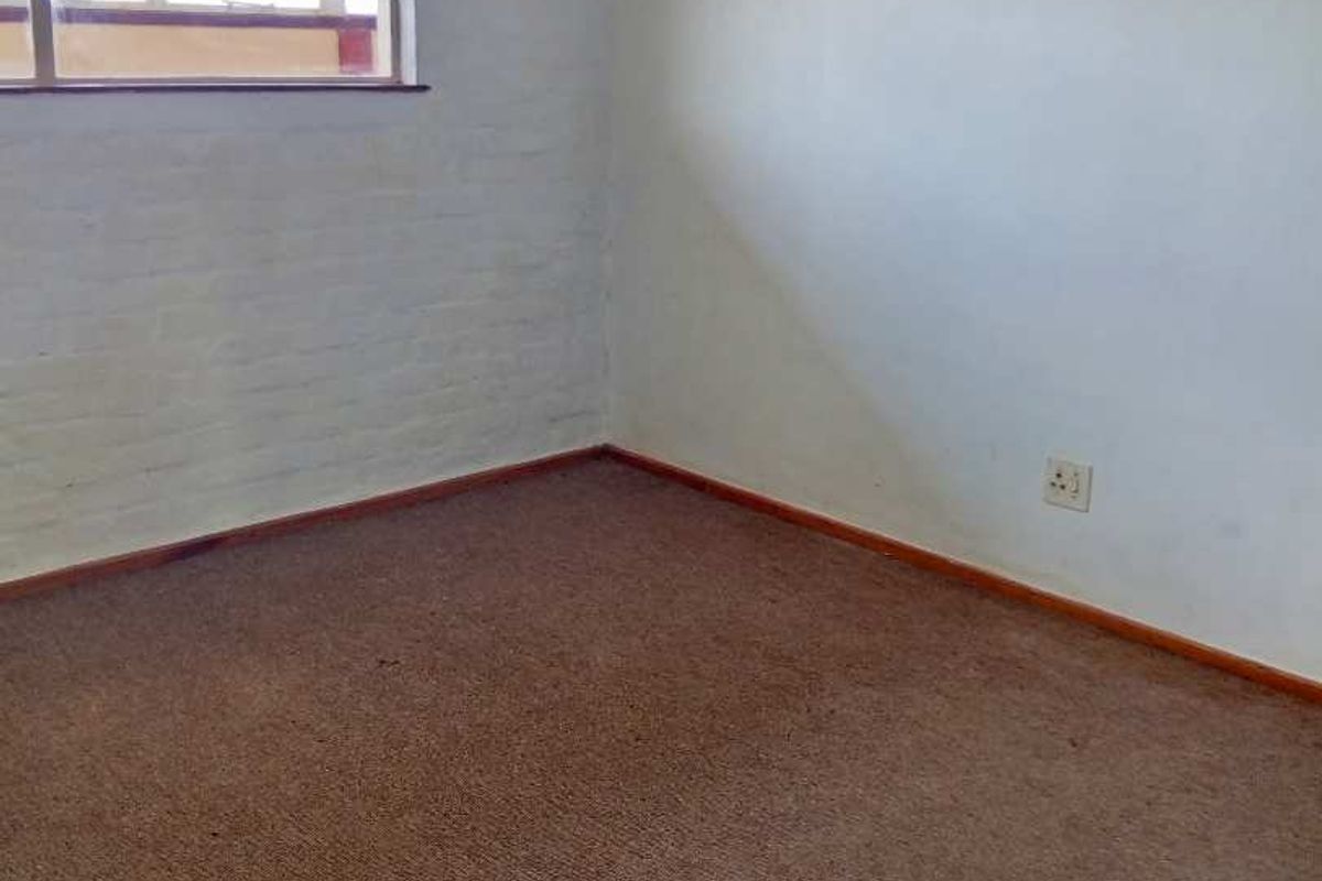 An empty bedroom featuring carpet flooring, a painted brick wall, and a window, offering a blank canvas for renovation.