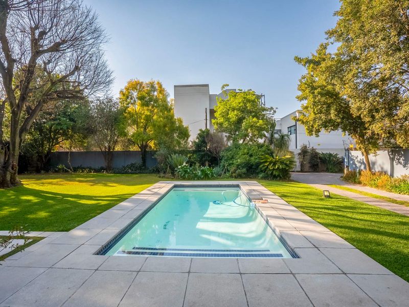 A well-maintained swimming pool set within a landscaped garden, featuring paved surrounds and mature trees, providing a private outdoor recreational space.