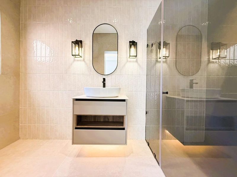 Modern bathroom featuring a floating vanity with a vessel sink, wall-mounted faucet, elegant wall sconces, and a glass-enclosed shower with neutral tiling.