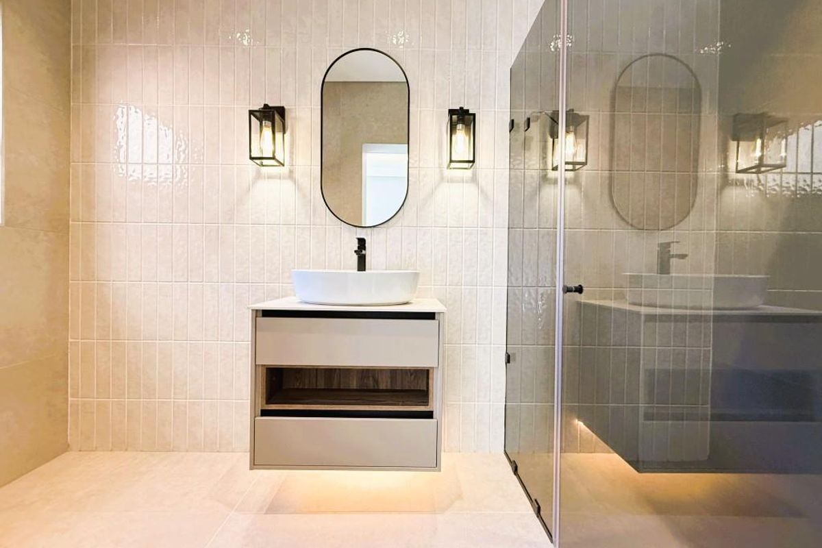 Modern bathroom featuring a floating vanity with a vessel sink, wall-mounted faucet, elegant wall sconces, and a glass-enclosed shower with neutral tiling.