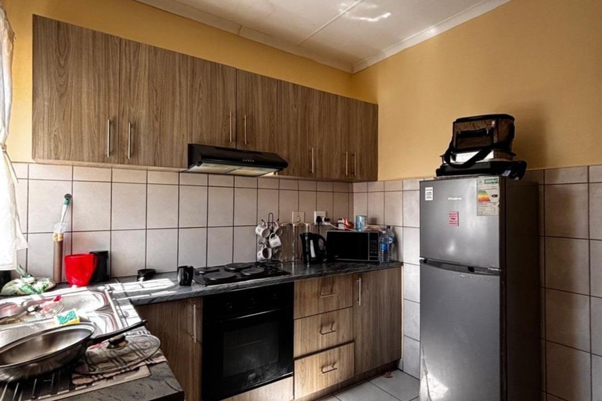 Compact kitchen featuring wood-look cabinetry, tiled splashbacks, built-in oven, hob, and extractor fan with tiled flooring.