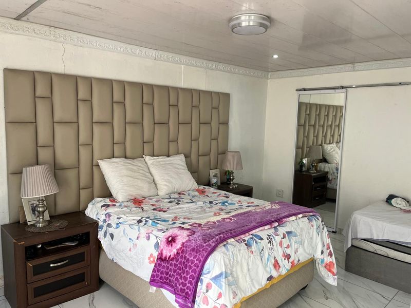 Bedroom featuring a large upholstered headboard, tiled flooring, and a sliding mirror door, with some visible wear on the wall and ceiling finishes.