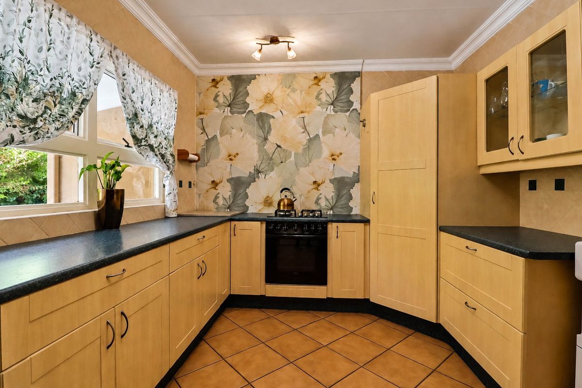 A functional kitchen featuring light wood cabinetry, dark countertops, a built-in oven with gas hob, and decorative floral wallpaper accents.