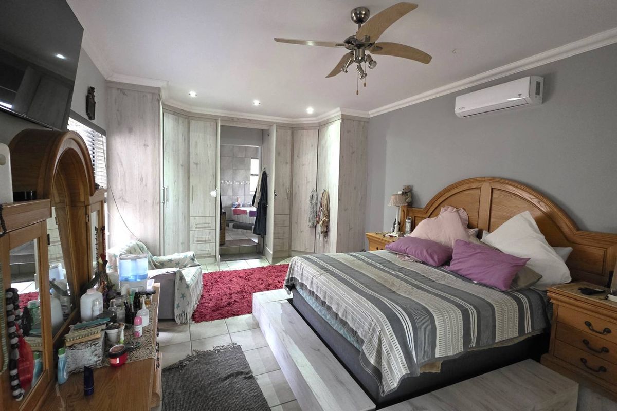 Spacious bedroom featuring extensive built-in cabinetry, tiled flooring, a ceiling fan, and a wall-mounted air conditioning unit.