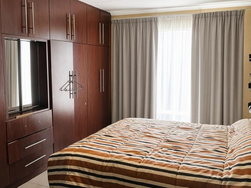 A well-maintained bedroom featuring extensive dark wood built-in cupboards, tiled flooring, and neutral curtains.