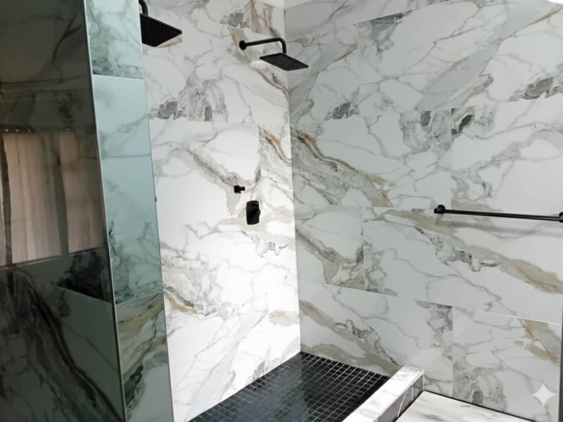 Modern walk-in shower featuring elegant marble-look wall tiles, black mosaic floor tiling, and contemporary black fixtures.