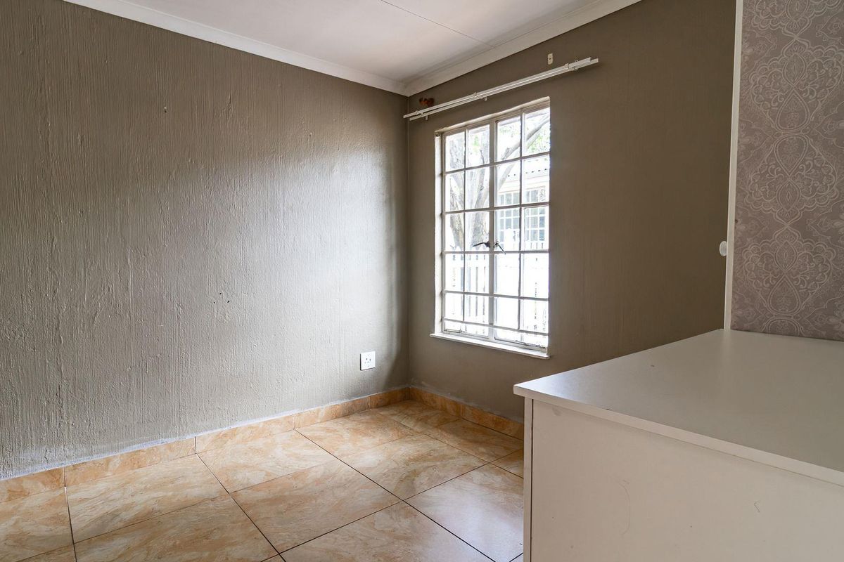 An empty bedroom featuring tiled flooring, a window with security bars, and neutral wall finishes, offering a blank canvas for personalization.