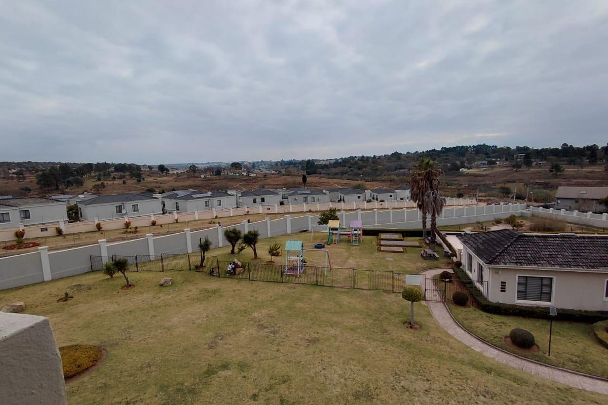 An elevated aerial view of a residential complex featuring a landscaped garden, perimeter fencing, and surrounding neighborhood landscape.