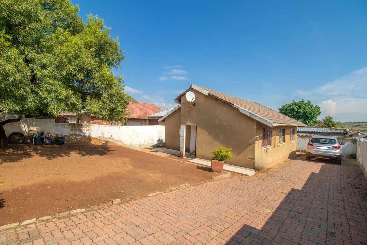 Rear exterior view of the property featuring a paved driveway, boundary wall, and tiled roof structure.