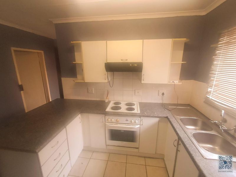 A functional kitchen featuring built-in cabinetry, an electric hob, oven, extractor fan, and a double bowl sink with tiled flooring.