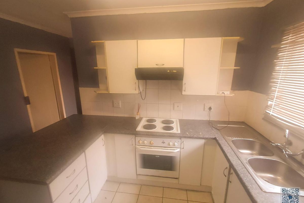 A functional kitchen featuring built-in cabinetry, an electric hob, oven, extractor fan, and a double bowl sink with tiled flooring.