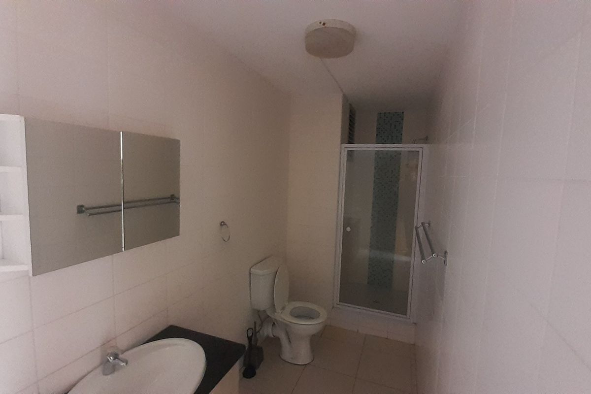 A functional bathroom featuring a built-in vanity, a toilet, and a separate shower enclosure with tiled walls.
