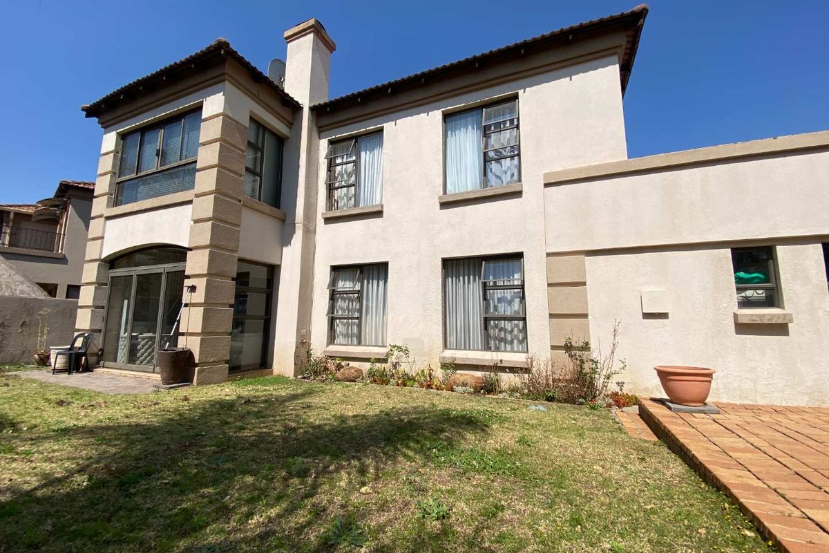 Rear elevation of a two-story house featuring a paved patio area, lawn, and large windows with a stucco finish.