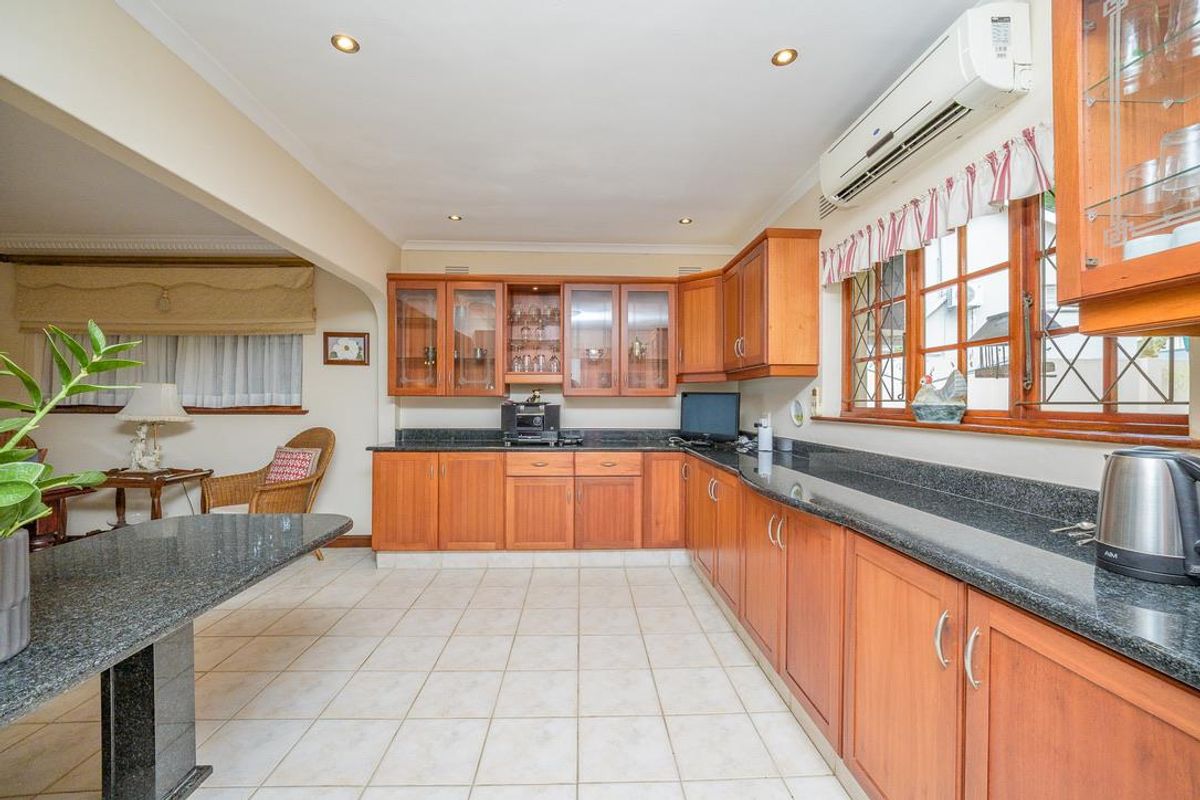 A functional kitchen featuring timber cabinetry, dark granite countertops, tiled flooring, and a wall-mounted air conditioning unit.