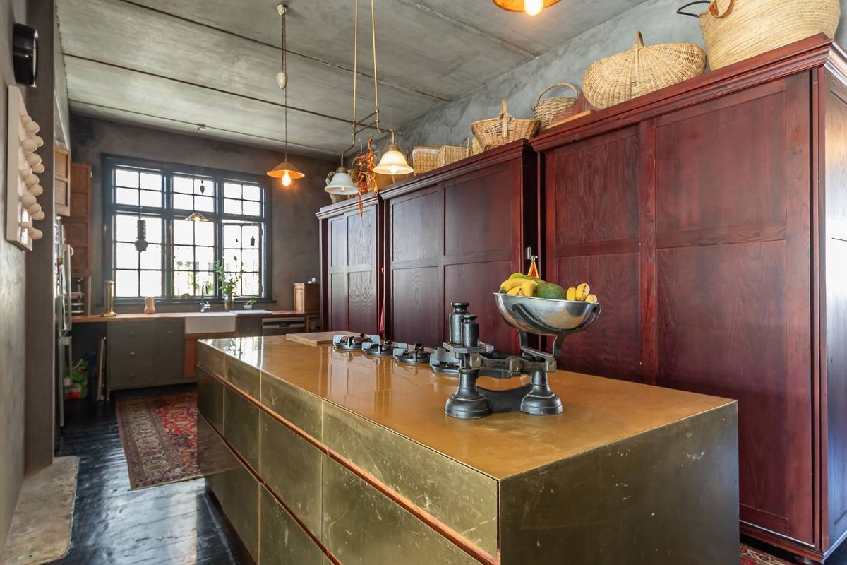 A sophisticated kitchen featuring a custom brass island with integrated gas hob, dark wood cabinetry, and an exposed concrete ceiling.