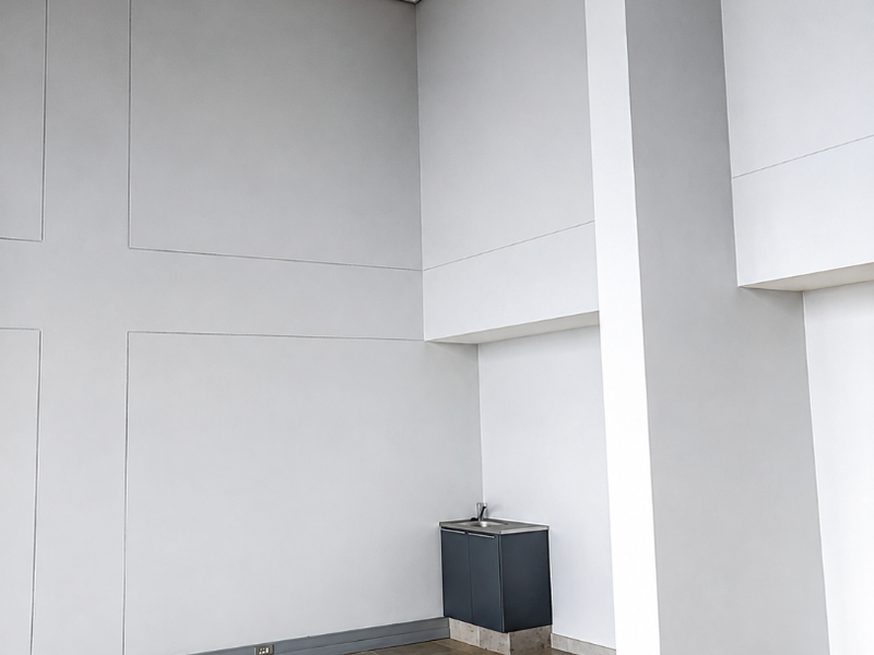 A spacious, empty retail utility area featuring high ceilings, tiled flooring, and a compact built-in kitchenette unit with a sink.