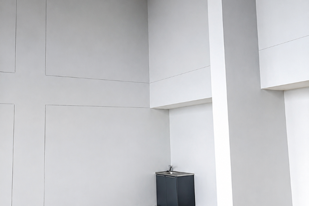 A spacious, empty retail utility area featuring high ceilings, tiled flooring, and a compact built-in kitchenette unit with a sink.