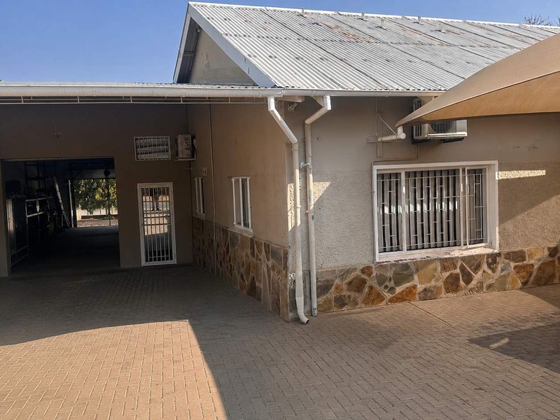 Rear exterior view of the business property featuring stone cladding, paved courtyard area, security bars on windows, and corrugated metal roofing.