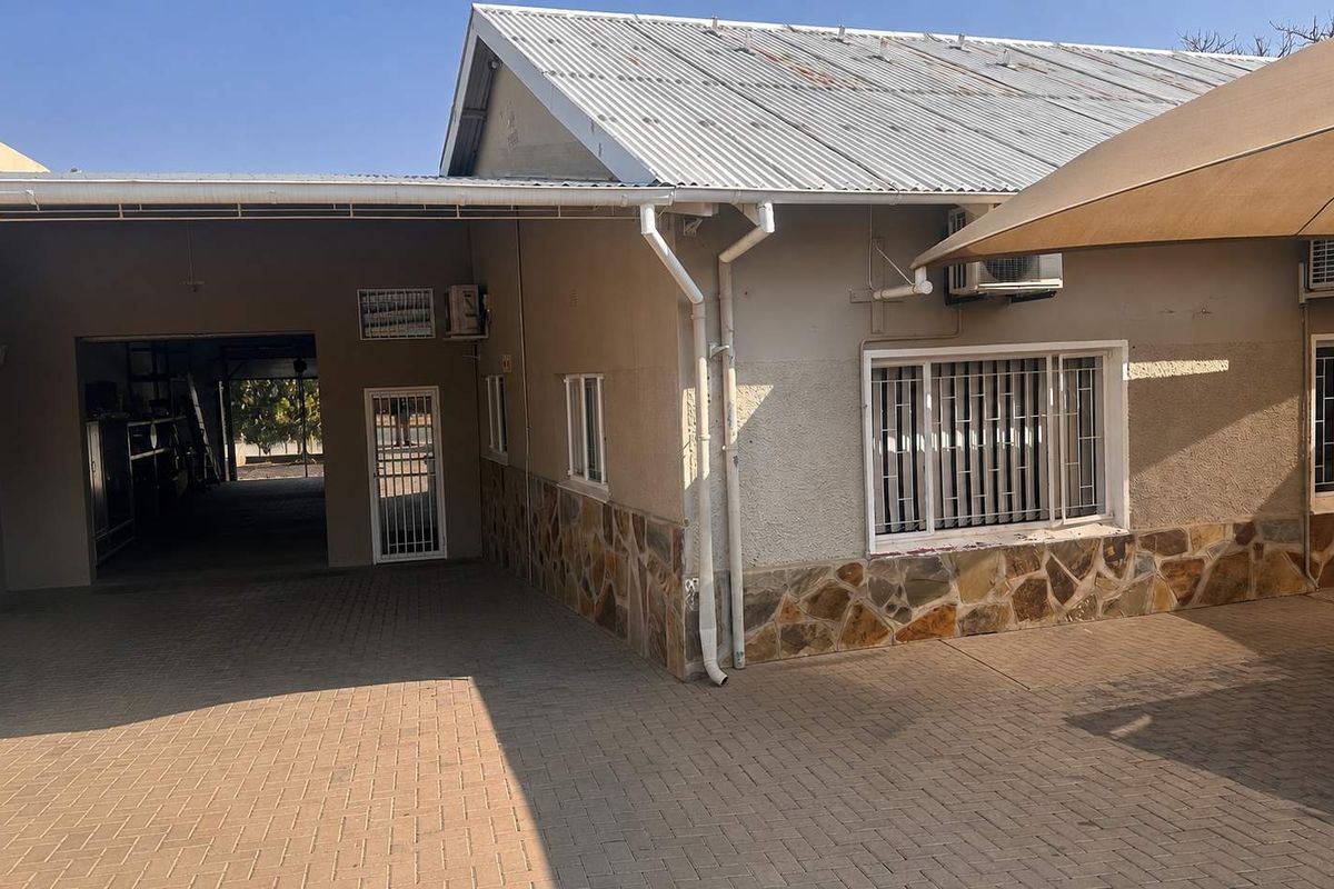 Rear exterior view of the business property featuring stone cladding, paved courtyard area, security bars on windows, and corrugated metal roofing.