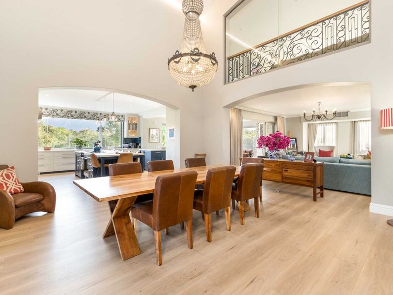 Spacious open-plan living and dining area featuring high ceilings, a grand crystal chandelier, and a mezzanine level with decorative wrought iron railings.