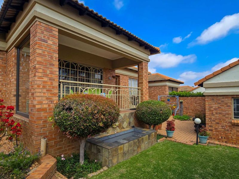 A well-maintained rear exterior view of the townhouse featuring a covered patio, brick facade, and a landscaped garden with a stone-clad water feature.