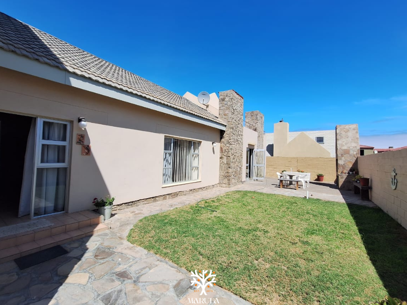 A well-maintained rear exterior view featuring a paved patio area, a small lawn, and stone-clad architectural accents against a clear blue sky.