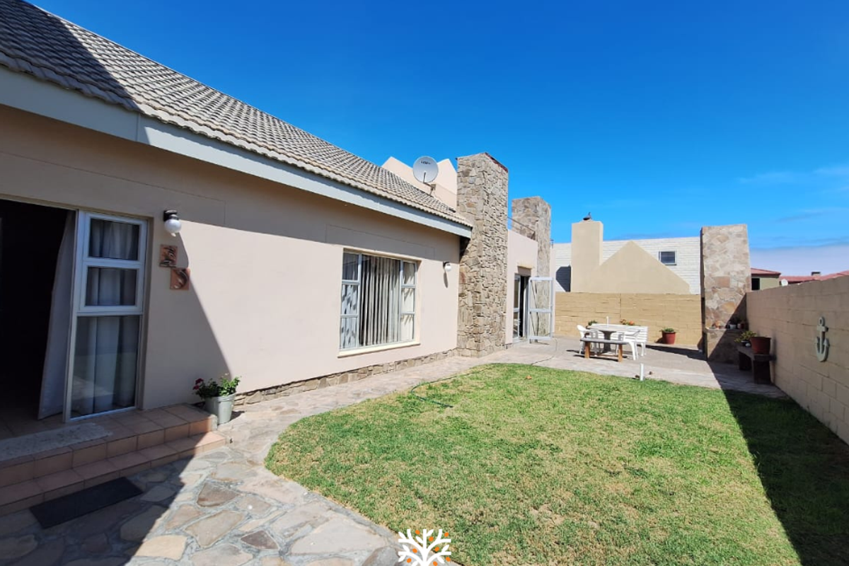 A well-maintained rear exterior view featuring a paved patio area, a small lawn, and stone-clad architectural accents against a clear blue sky.