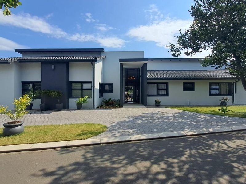 Modern single-story residence featuring a paved driveway, clean architectural lines, dark-framed windows, and a well-maintained front garden.