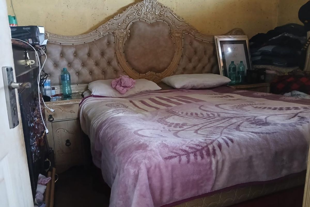 A bedroom featuring a large ornate headboard and basic wall finishes, requiring cosmetic updates to improve the overall aesthetic and condition.