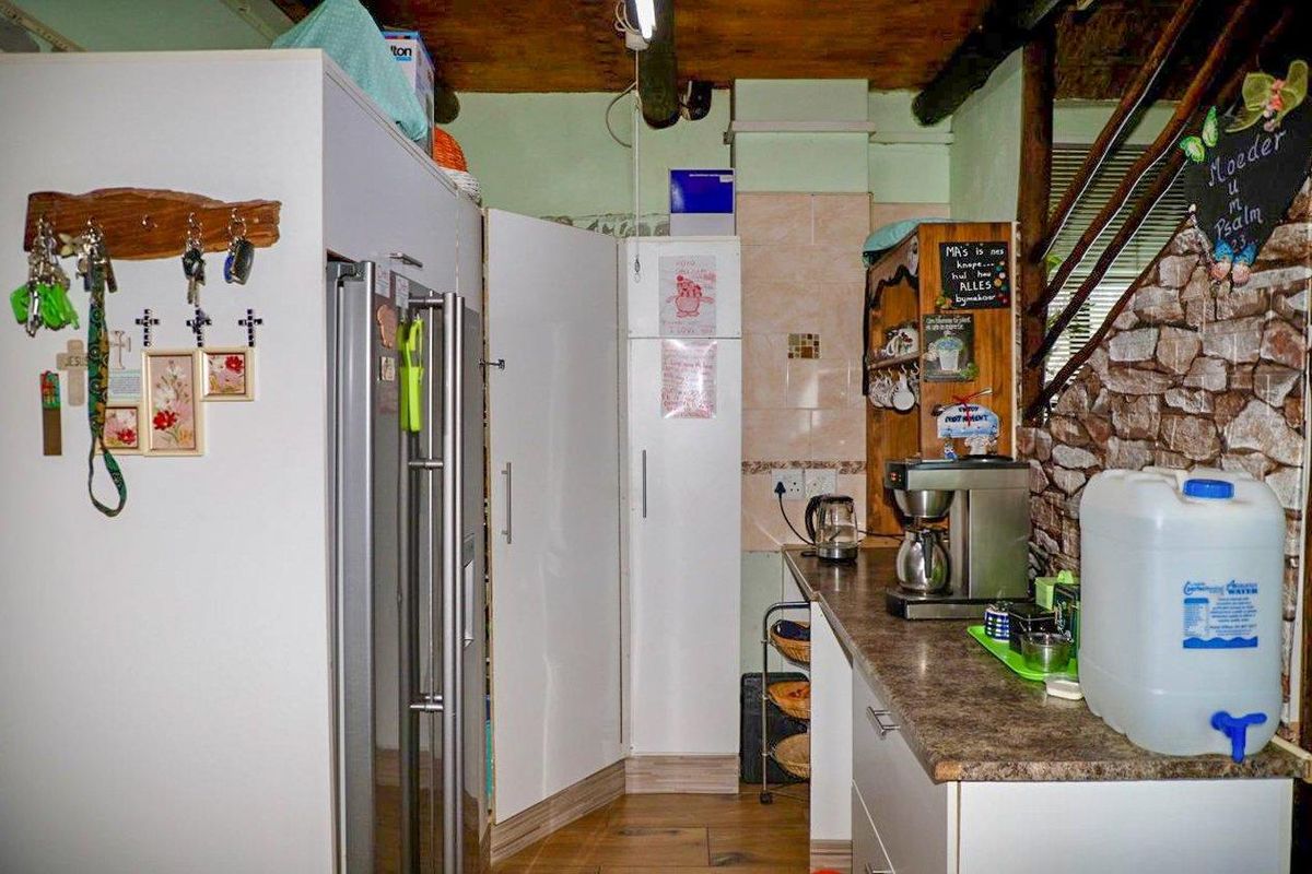 A compact kitchen area featuring laminate countertops, built-in cabinetry, and a stone-clad feature wall with an adjacent staircase.