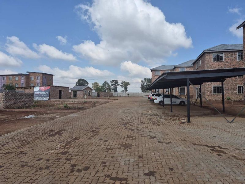 Exterior view of an apartment complex featuring facebrick buildings, a paved driveway, and covered parking carports.