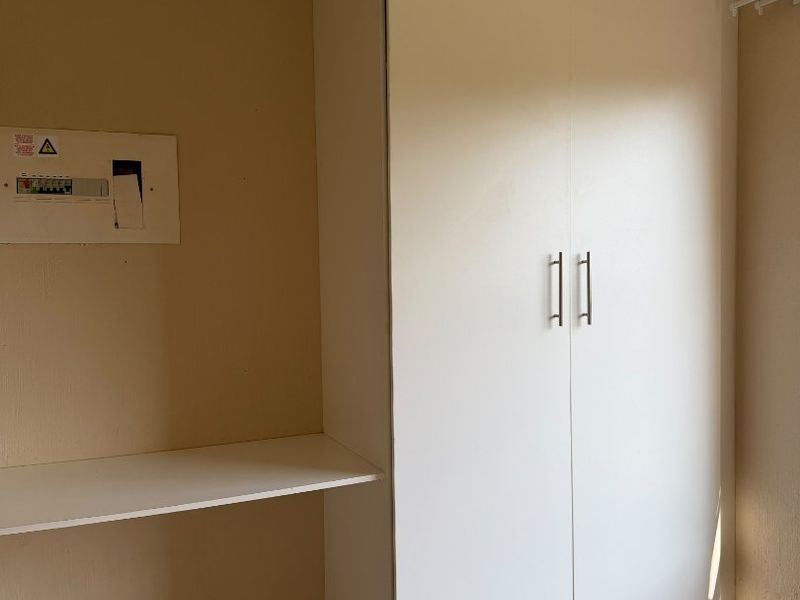 A functional bedroom space featuring a white built-in wardrobe, tiled flooring, and a wall-mounted electrical distribution board.