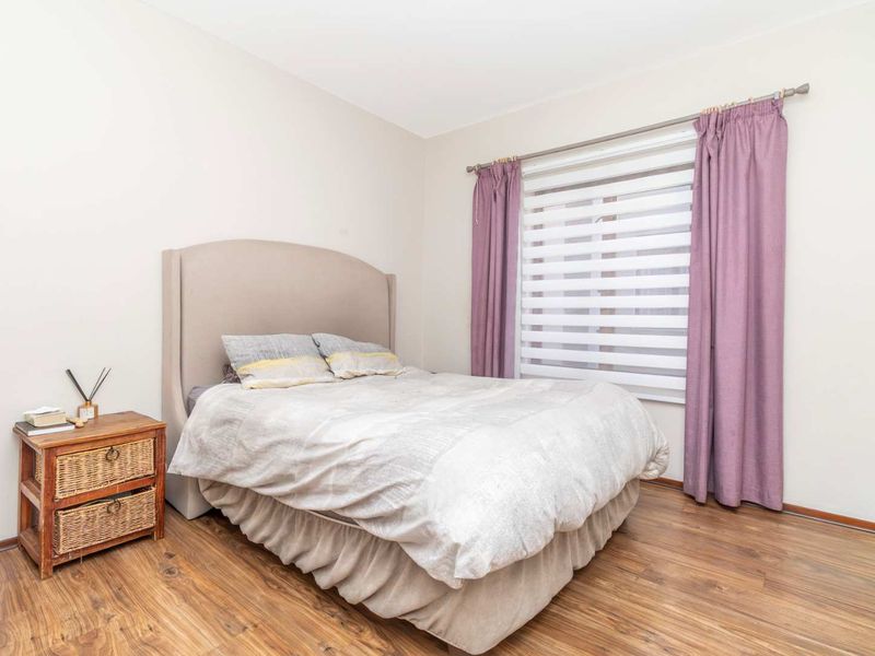 A well-maintained bedroom featuring durable laminate flooring and a window fitted with both blinds and curtains.