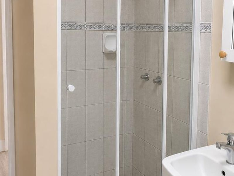 A functional bathroom featuring a tiled shower enclosure with a sliding door, a pedestal basin with a mixer tap, and neutral wall tiling.